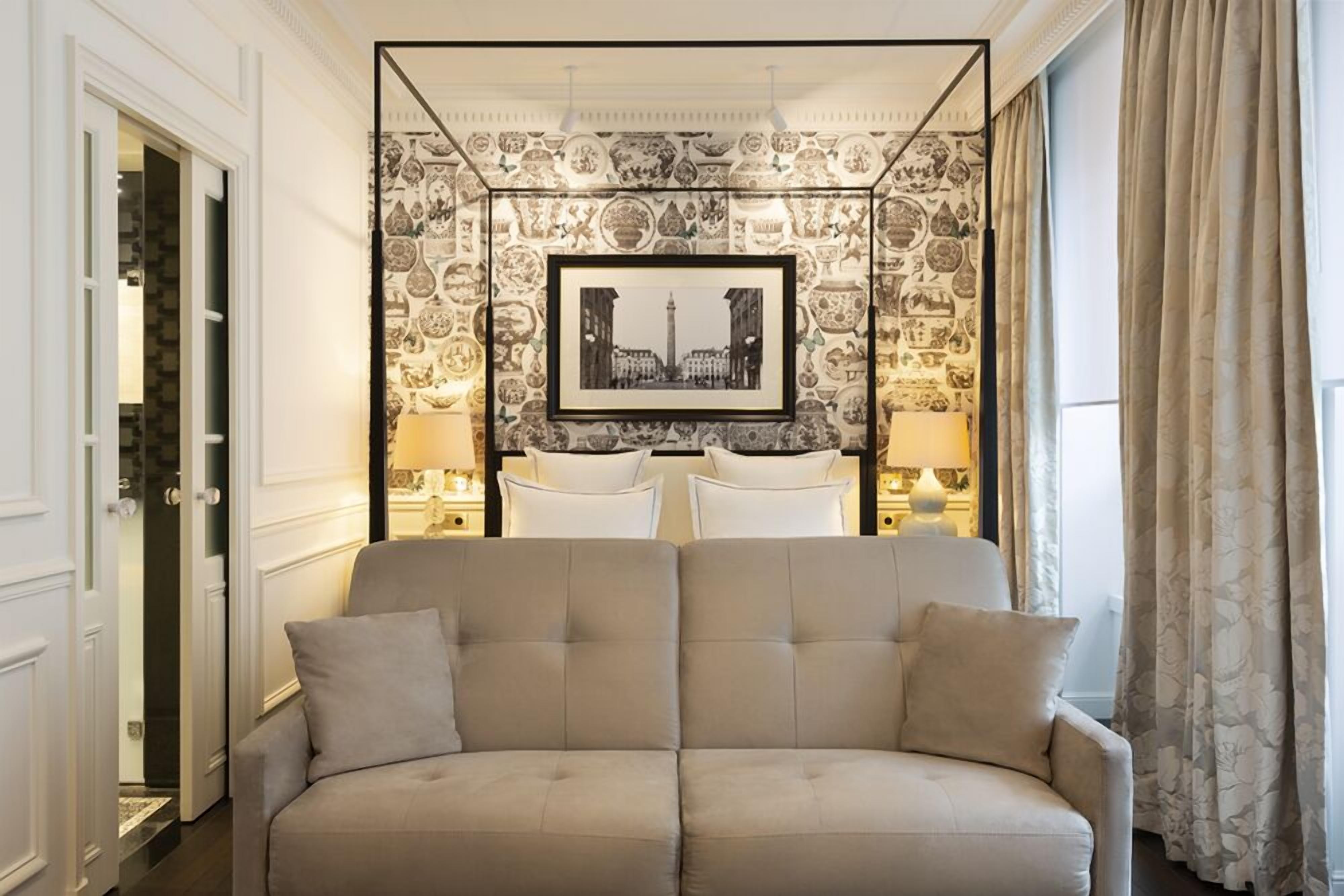 A modern living room with a beige sofa, a framed black and white cityscape picture, and patterned wallpaper.
