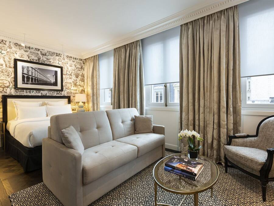 Habitación de hotel con cama, sofá, sillón y mesa de centro con libros y flores.