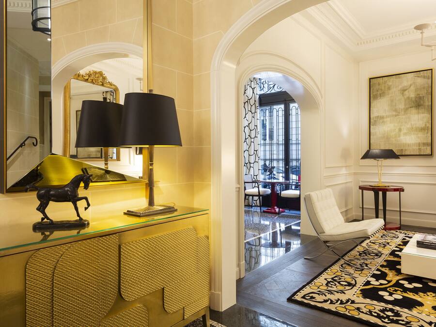 Un hall d’hôtel avec un bureau dont le plateau est en verre, une sculpture équestre noire, un grand miroir et un tapis à motifs.