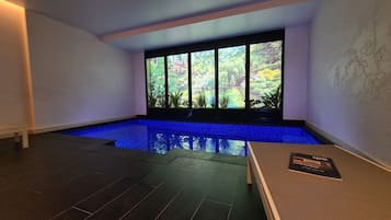 Una piscina interior moderna con vistas a un jardín a través de amplios ventanales.