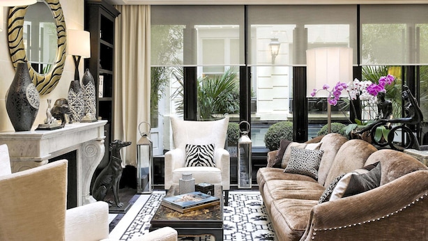 A well-lit living room with a fireplace, a white armchair, a brown sofa, and decorative vases. - Hôtel Keppler (Paris)