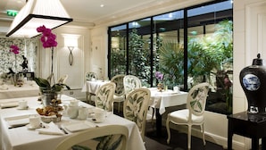 A dining area with tables set for service, chairs with floral upholstery, a large window with a view of greenery, and a decorative vase on a table. - Hôtel Keppler (Paris)