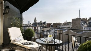 A balcony with a white lounge chair, a small table with a pitcher of lemonade, and a view of the Eiffel Tower. - Hôtel Keppler (Paris)