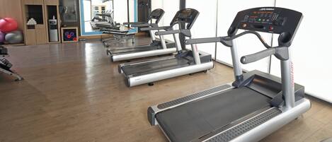 Un gimnasio con cintas de correr, pelotas de ejercicio y un espejo.