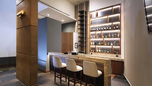 Zona de bar con encimera de granito, taburetes y una estantería con botellas de vino.