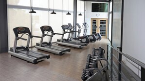 Un gimnasio con cintas de correr, elípticas y una banca para pesas.