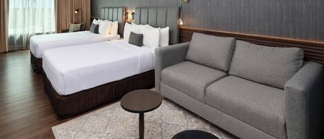 Habitación de hotel con dos camas, un sofá, una mesita y una alfombra estampada.