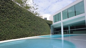 Un edificio moderno con piscina, seto y ventanas amplias.