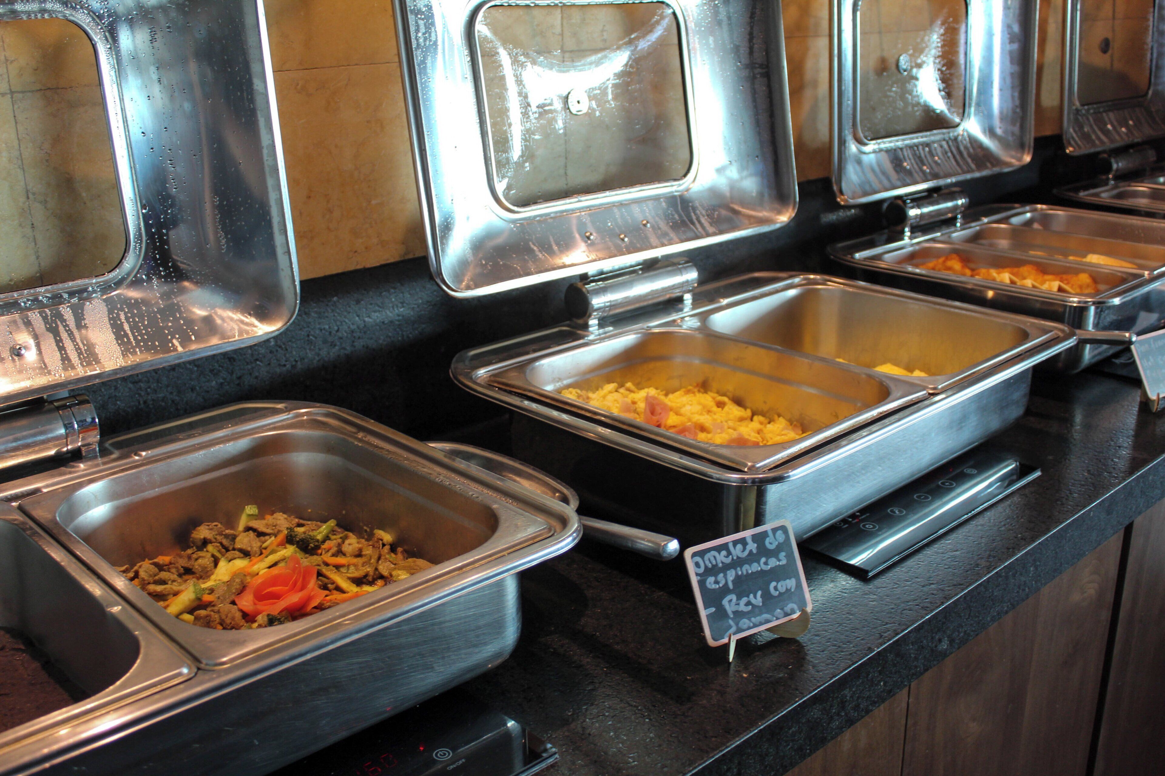Un bufé con diversas opciones de comida en recipientes metálicos.