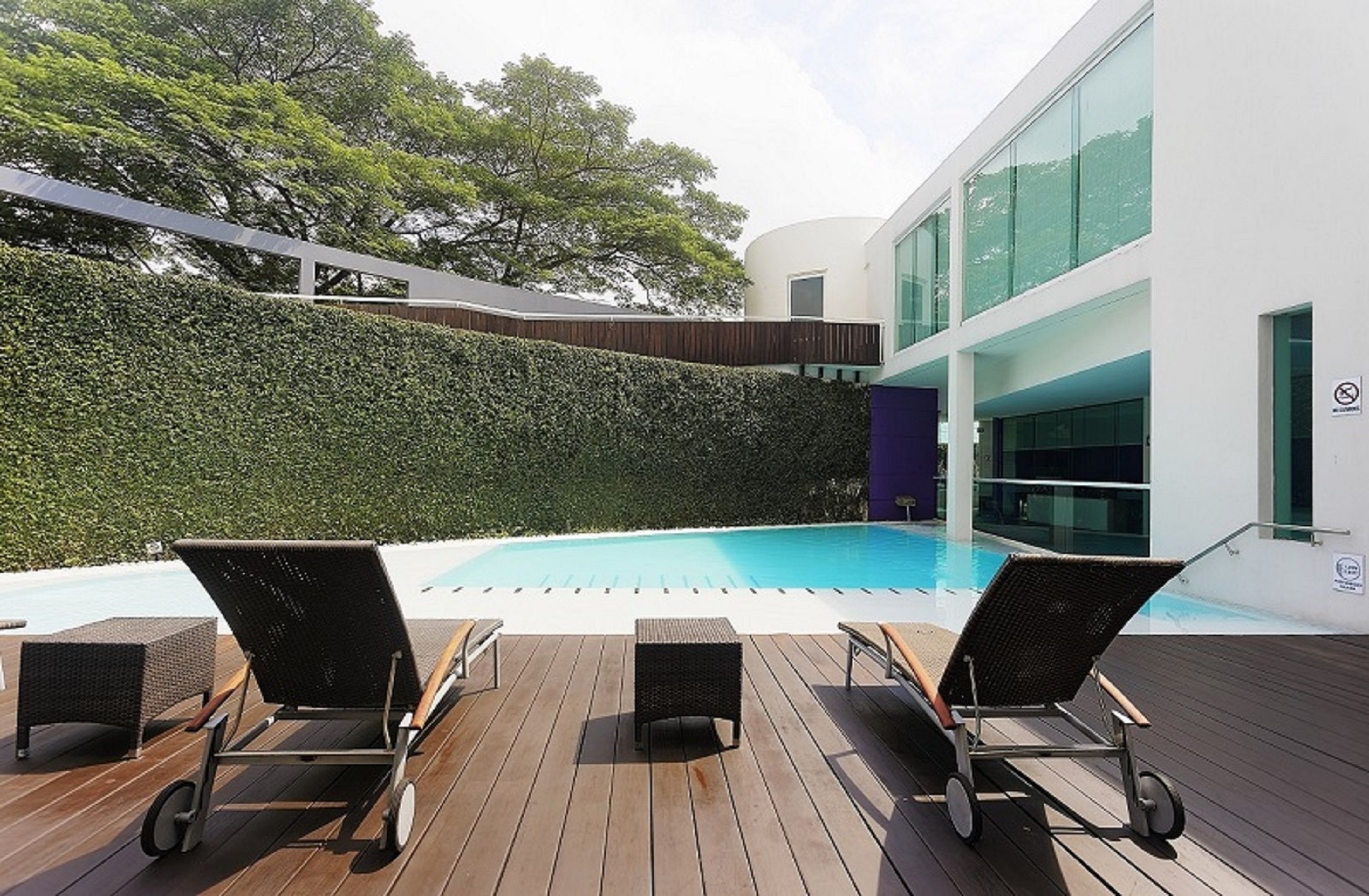 A modern outdoor pool area with lounge chairs and a wooden deck.
