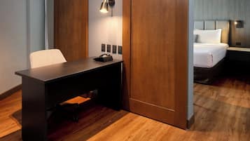 Habitación de hotel con escritorio, cama, lámpara de pared y puerta de madera.