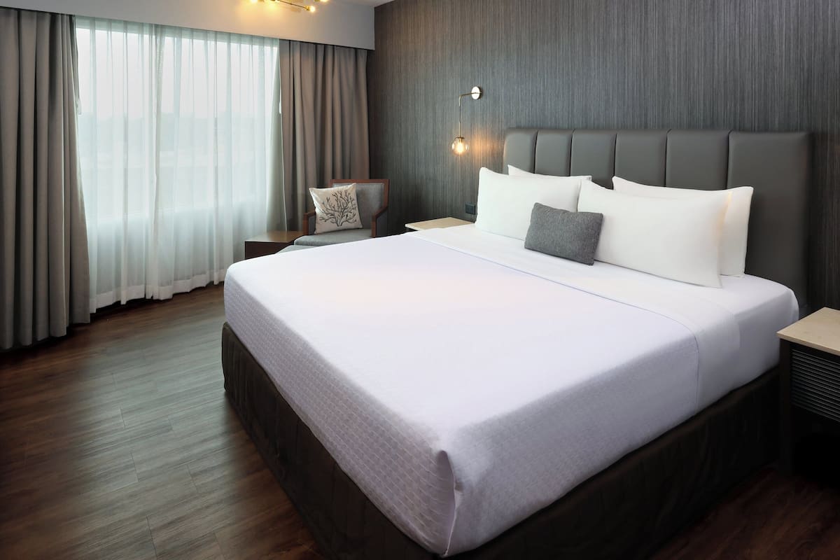 A hotel room with a large bed, a nightstand, a chair, and a wall-mounted lamp.