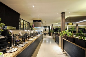 Un buffet avec plusieurs présentoirs de nourriture, un espace pour s’asseoir et des plantes en pot.