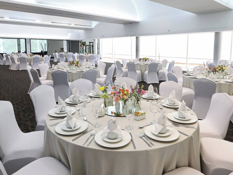 A banquet hall with round tables, white chairs, and floral centerpieces.