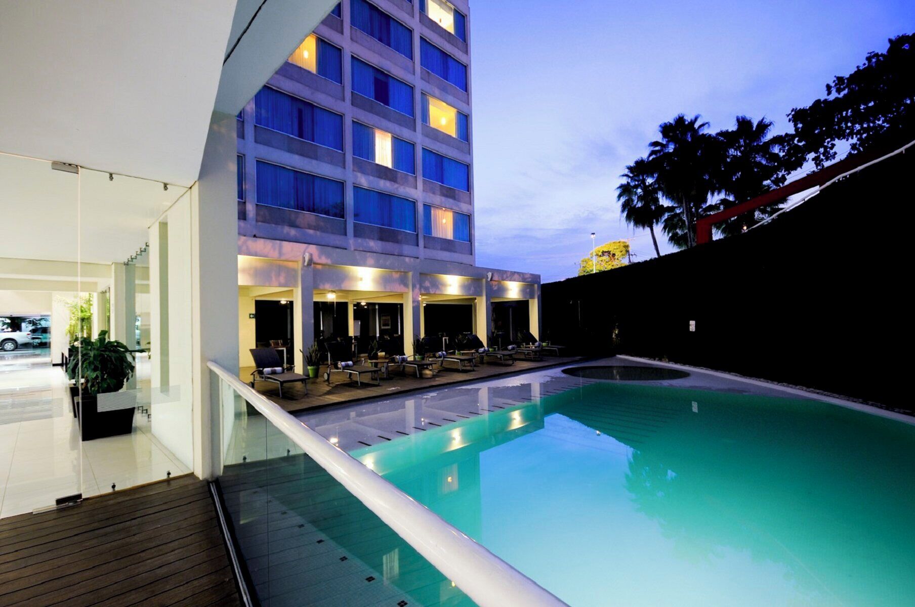 A hotel with a swimming pool, outdoor seating, and a multi-story building with illuminated windows.