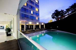 Un hôtel doté d’une piscine, d’un espace extérieur aménagé et d’un bâtiment à plusieurs étages dont les fenêtres sont illuminées.