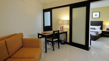 A hotel room with a sofa, a desk with a chair, a bed, and a nightstand.