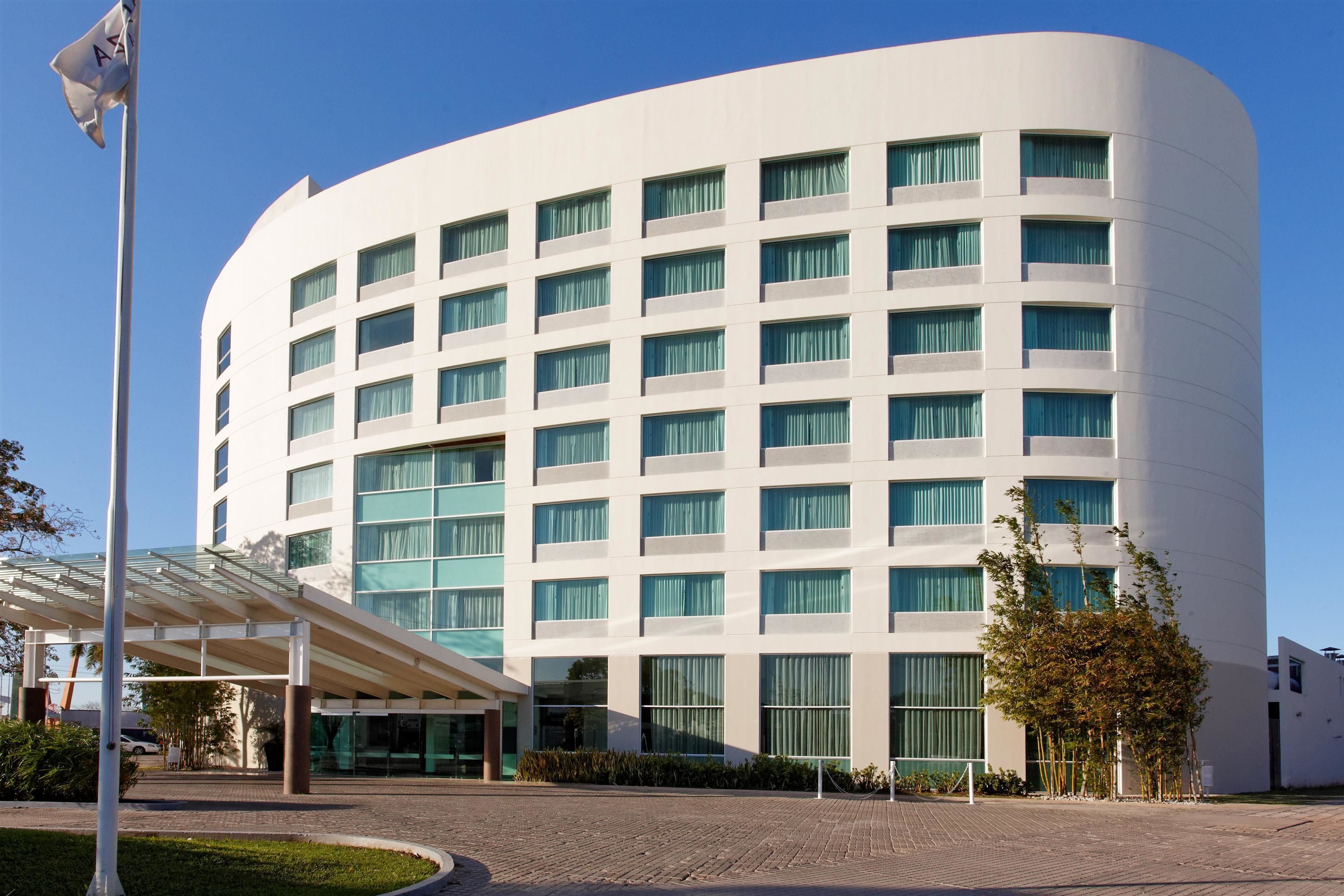 A modern hotel with a curved facade, large windows, and a covered entrance area.