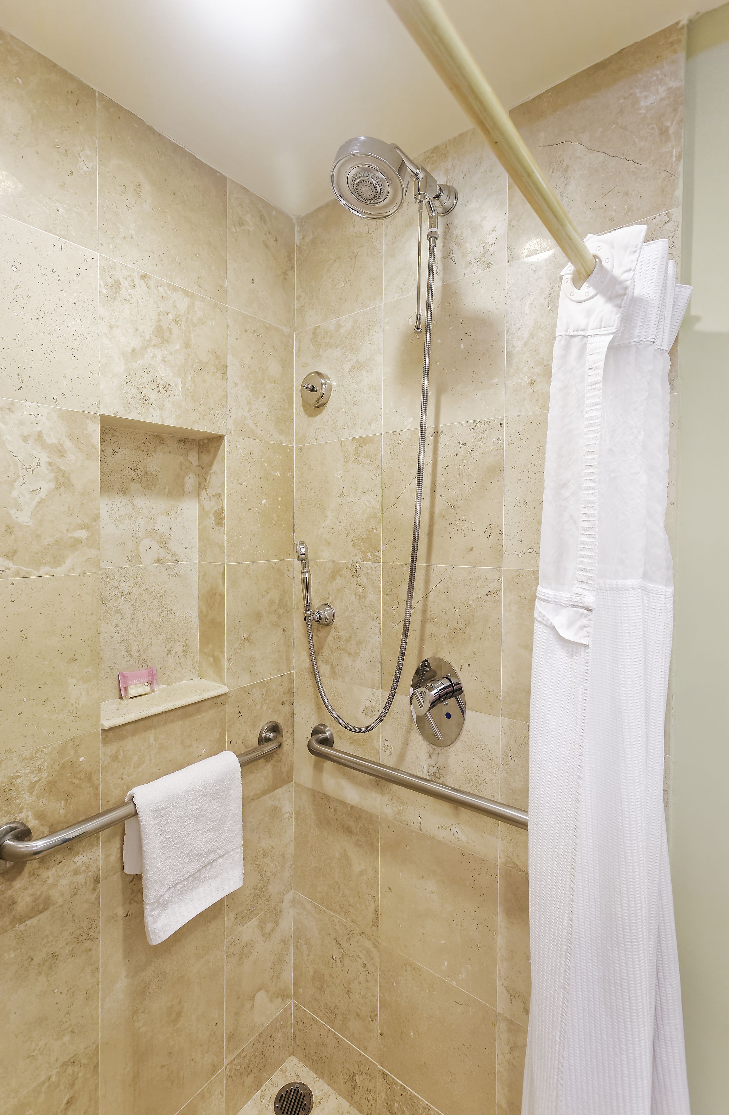 A shower area with beige tiles, a handheld showerhead, a towel rack, and a white towel.