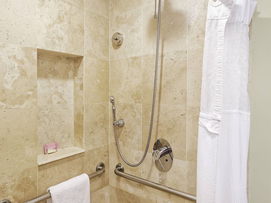 A shower area with beige tiles, a handheld showerhead, a towel rack, and a white towel.