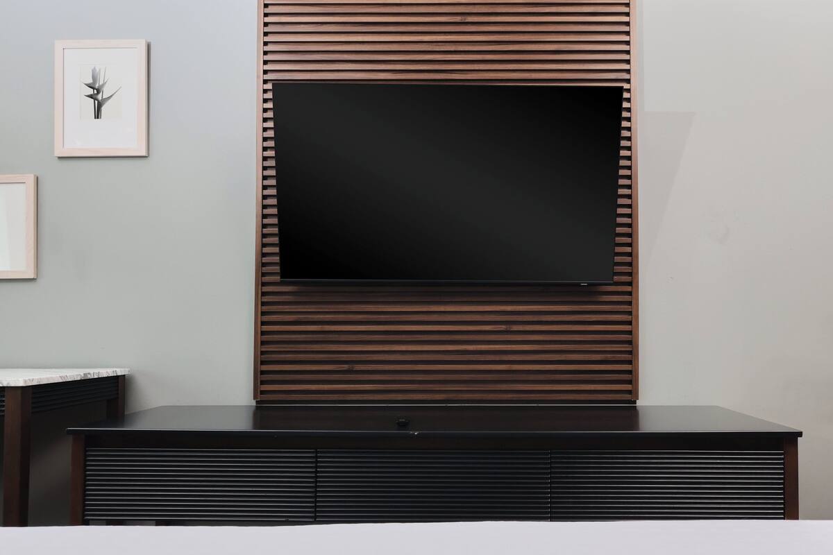 A modern living room with a flat-screen TV mounted on a wooden panel wall, a dark wooden entertainment unit below, and a framed picture on the wall.