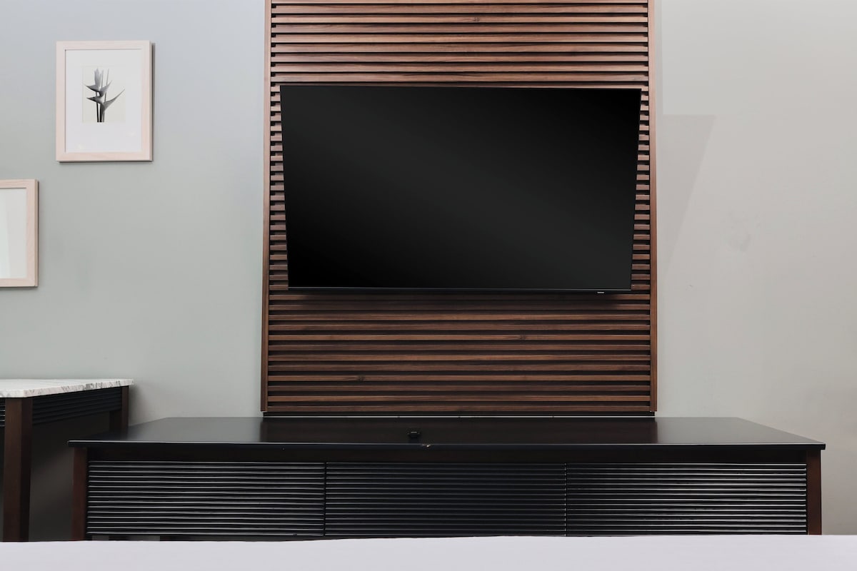 A modern living room with a flat-screen TV mounted on a wooden panel wall, a dark wooden entertainment unit below, and a framed picture on the wall.