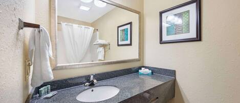 A bathroom with a granite countertop, a white sink, a large mirror, and a framed picture on the wall.