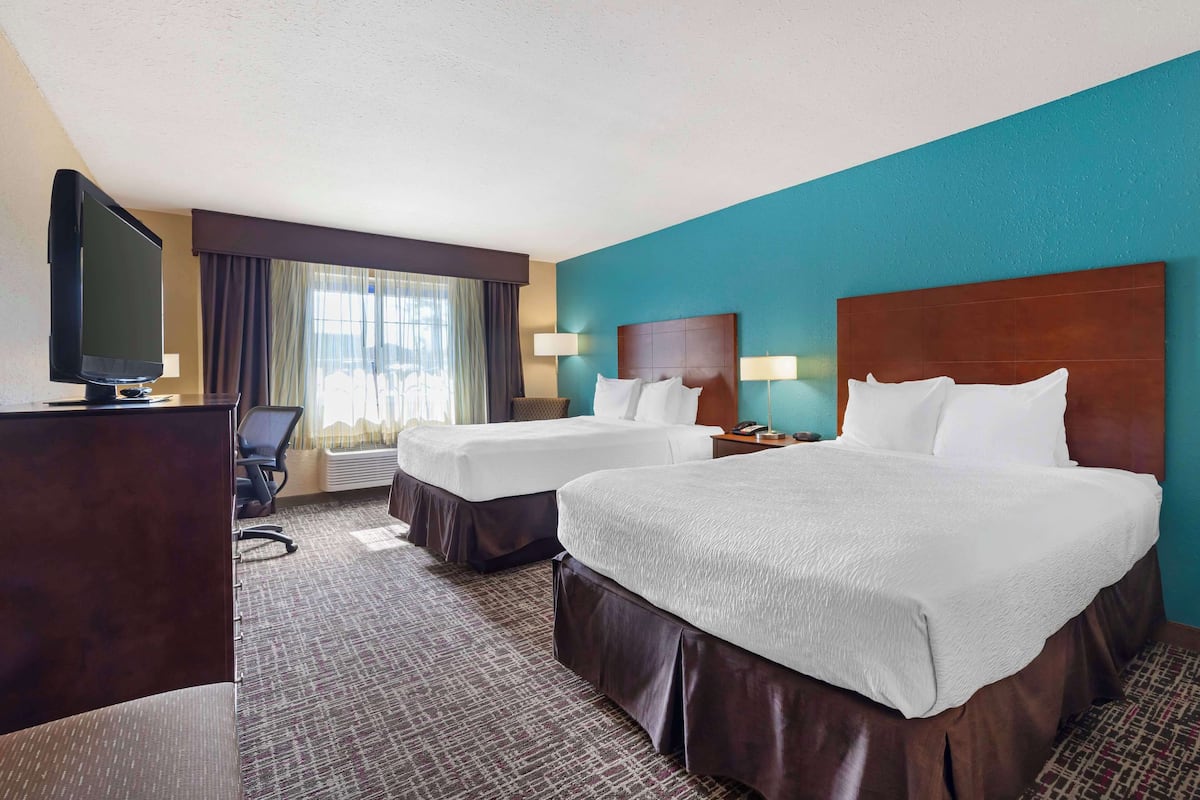 A hotel room with two beds, a desk, a television, and a window with curtains.