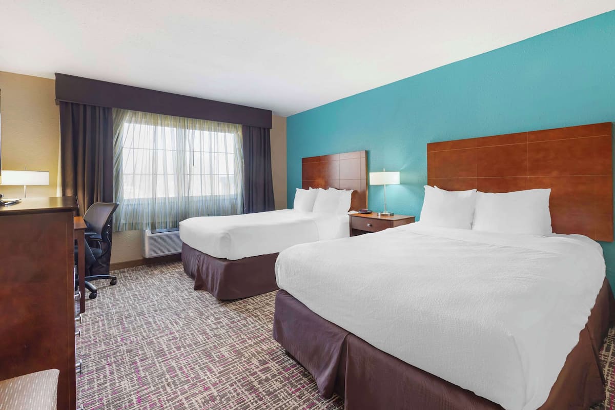A hotel room with two beds, a desk, a chair, a lamp, and a window with curtains.