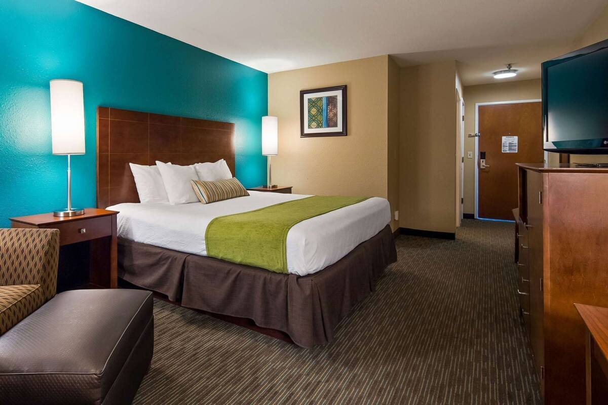 A hotel room with a bed, two bedside lamps, a chair, a desk, and a television.