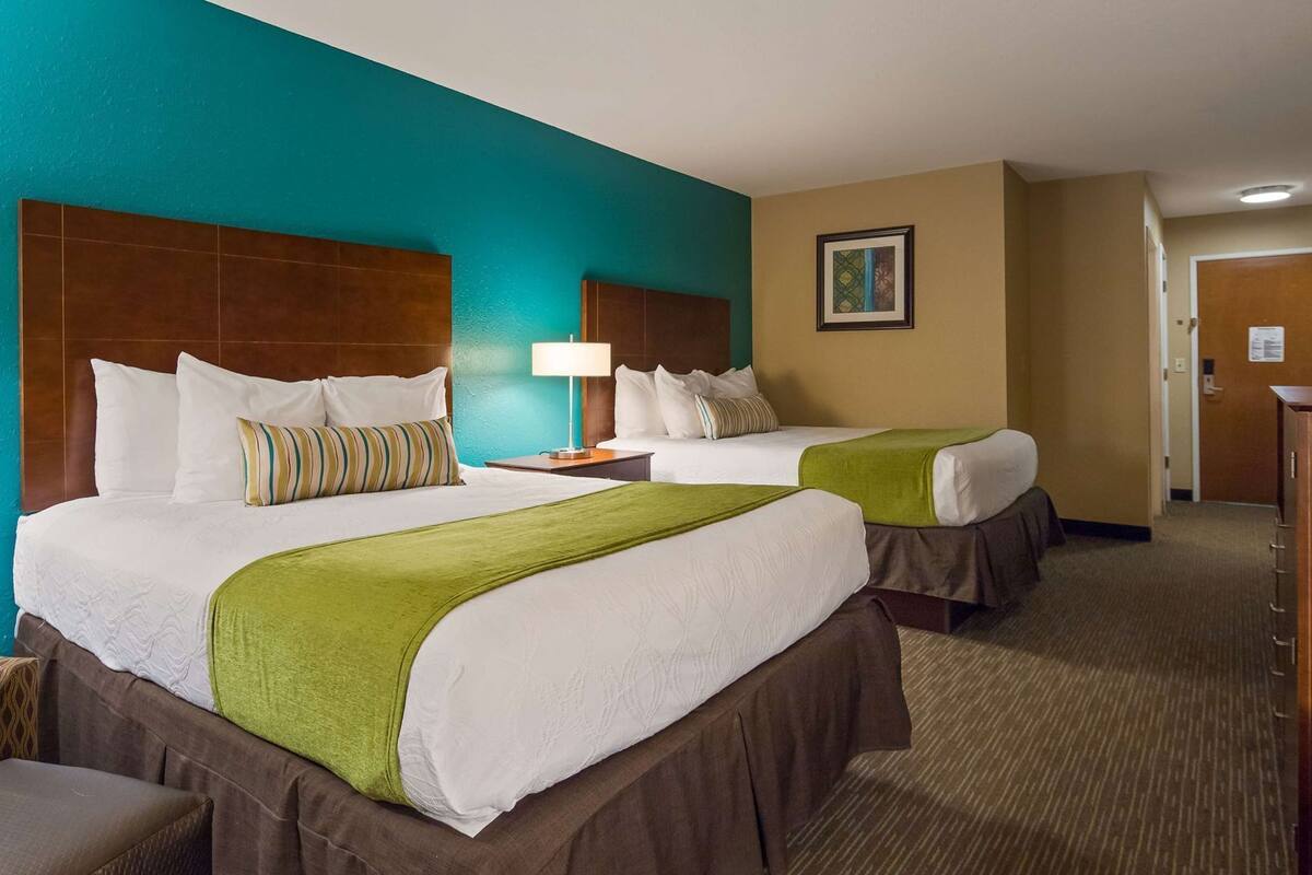 A hotel room with two beds, a desk, a chair, a television, and a painting on the wall.