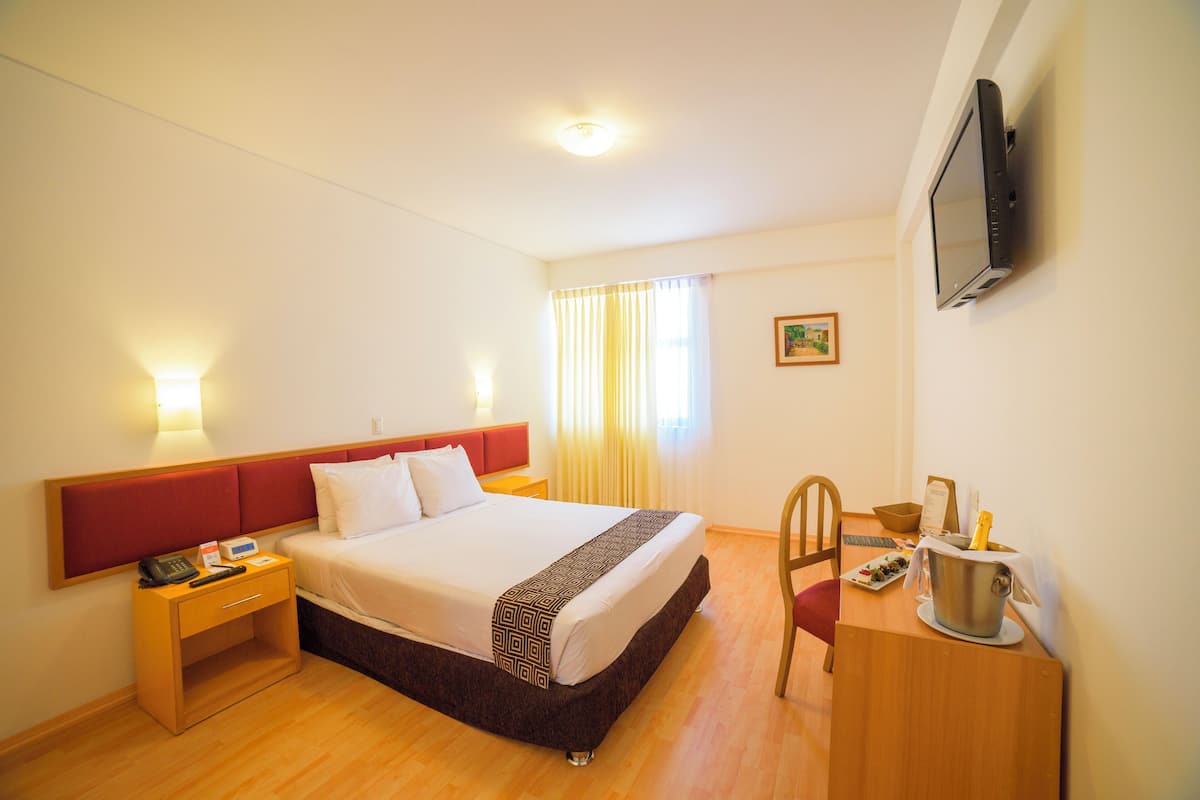 Une chambre d’hôtel comprenant un lit, une table de chevet, une télévision et un bureau avec une chaise.