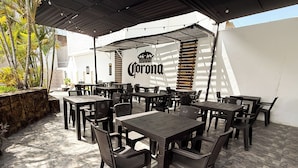 An outdoor patio area with multiple tables and chairs, a Corona logo on the wall, and a stone wall with plants. - WinMeier Hotel & Casino (Chiclayo)