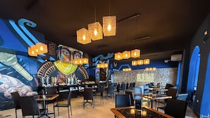 A restaurant interior with tiled floors, black chairs, wooden tables, hanging pendant lights, and a mural on the wall. - WinMeier Hotel & Casino (Chiclayo)