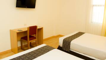 A hotel room with two beds, a desk, a chair, a TV, and a window with curtains.
