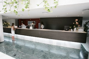 Un área de recepción con piso de mármol, un mostrador de recepción y una planta grande en maceta.