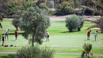 Un campo de golf con jugadores y bolsas sobre el césped, rodeado de árboles y arbustos.