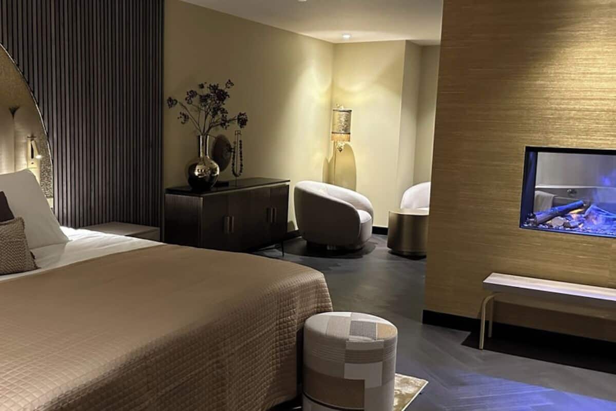 A modern hotel room with a large bed, a TV, a desk, and a chair.