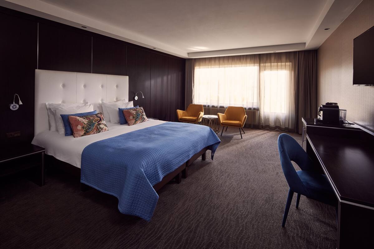 A hotel room with a large bed, two armchairs, a desk, and a TV.
