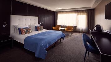 Una habitación de hotel con una cama grande, dos sillones, un escritorio y un televisor.