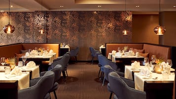 Un restaurante con mesas dispuestas para comer, que presenta una pared con diseño y luces colgantes.