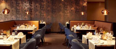 Un restaurante con mesas dispuestas para comer, que presenta una pared con diseño y luces colgantes.
