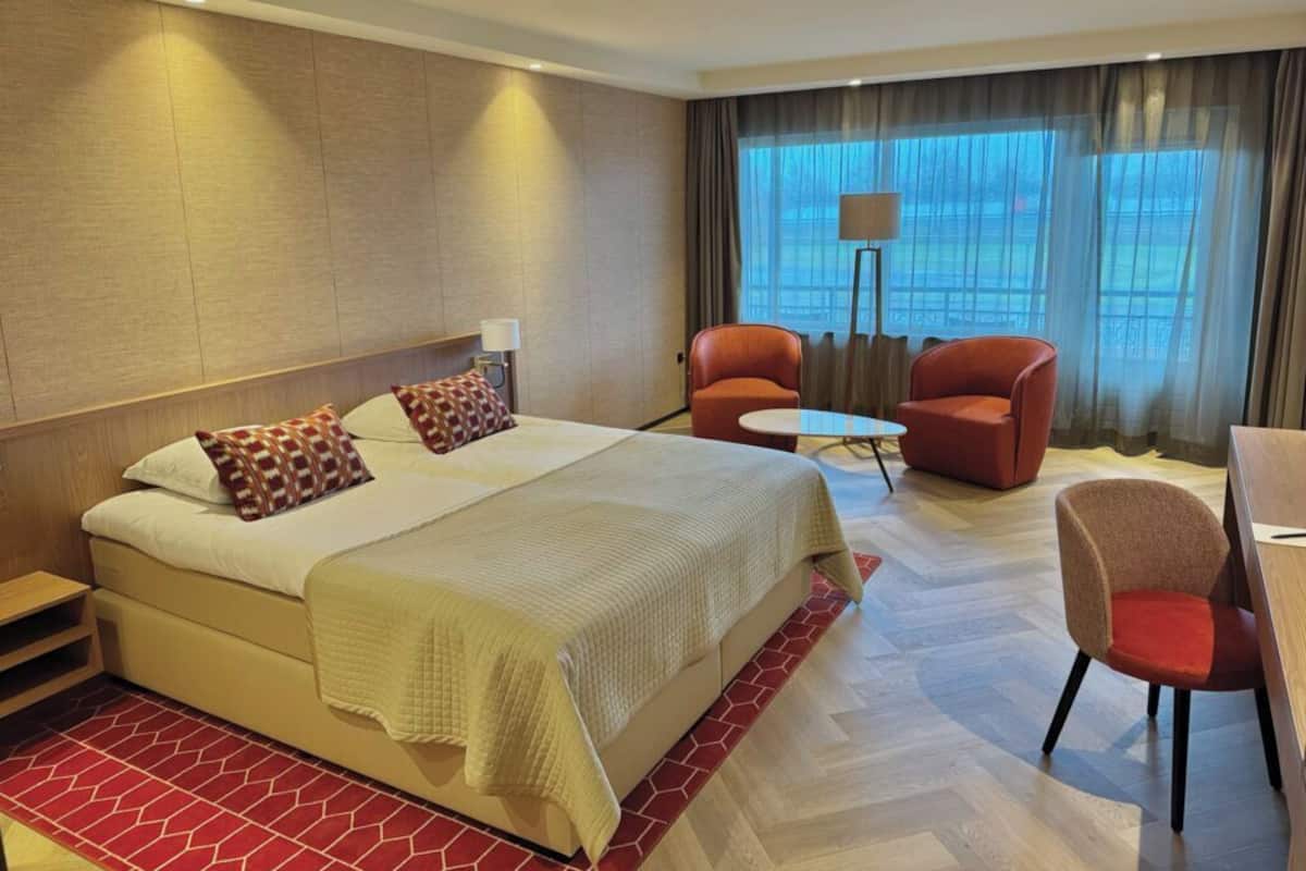 A hotel room with a bed, two armchairs, a small table, and a window with curtains.