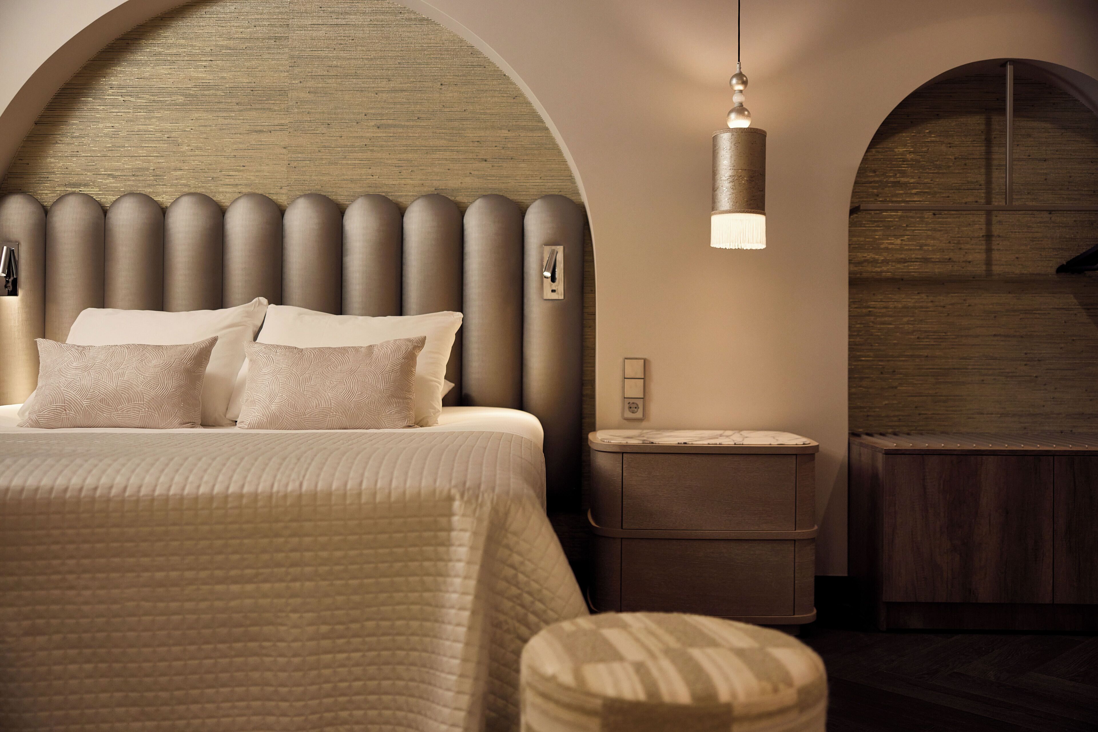 A modern bedroom with a large bed, a bedside table, a nightstand, and a hanging light fixture.