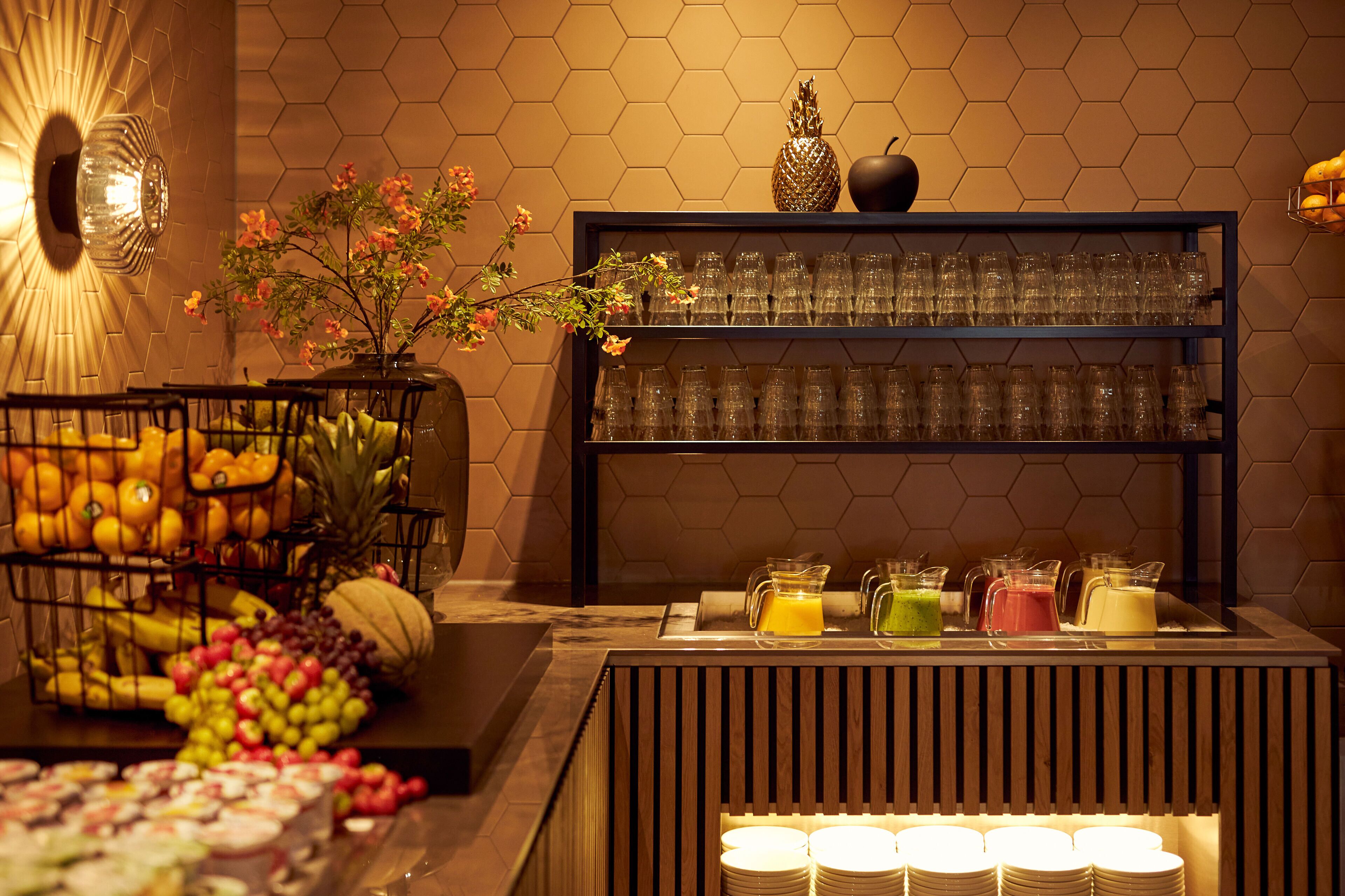 A breakfast buffet with fruits, a fruit basket, and a juice station.