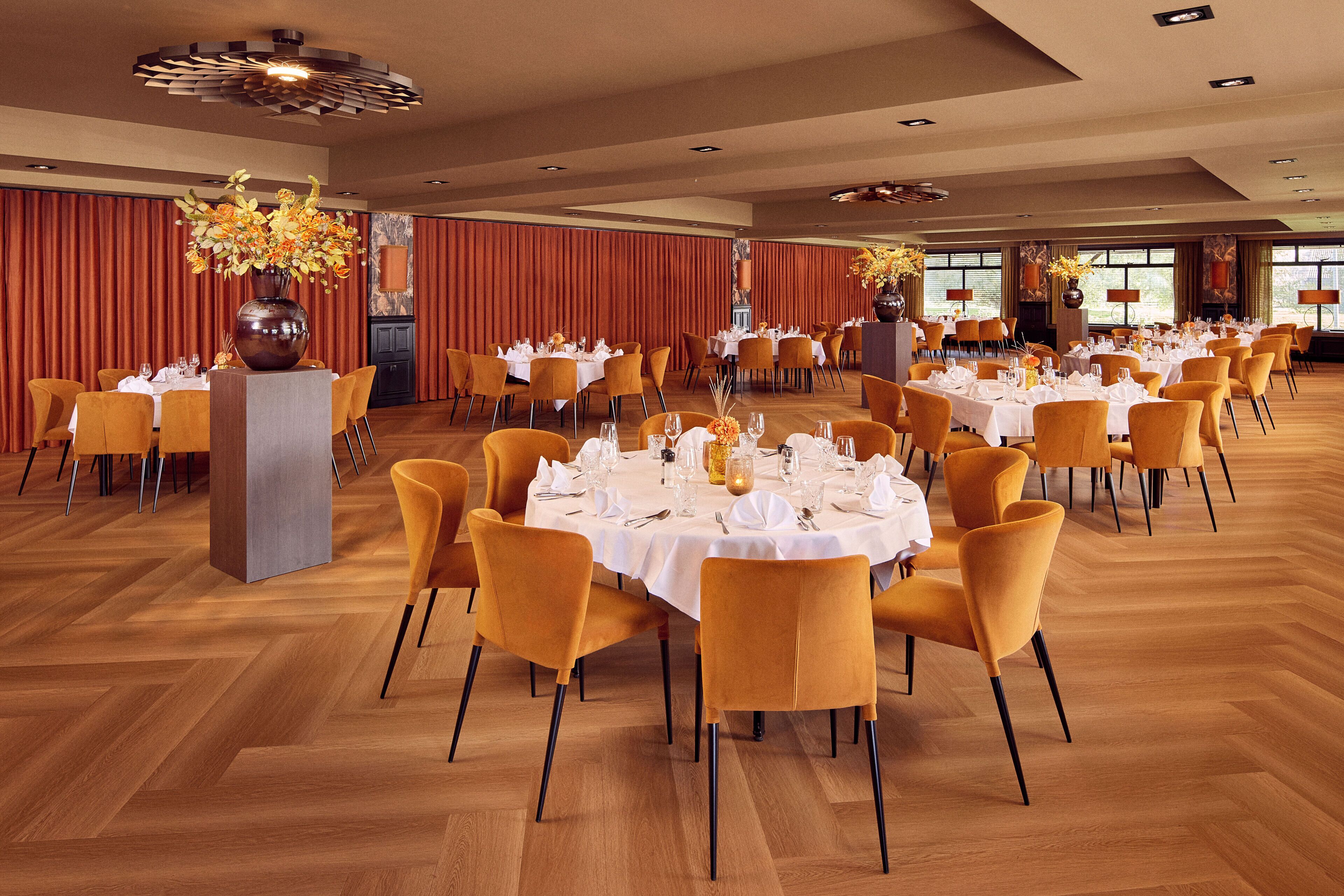 A spacious dining hall with multiple round tables set for dining, each with white tablecloths and yellow chairs.