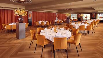 A spacious dining hall with multiple round tables set for dining, each with white tablecloths and yellow chairs.