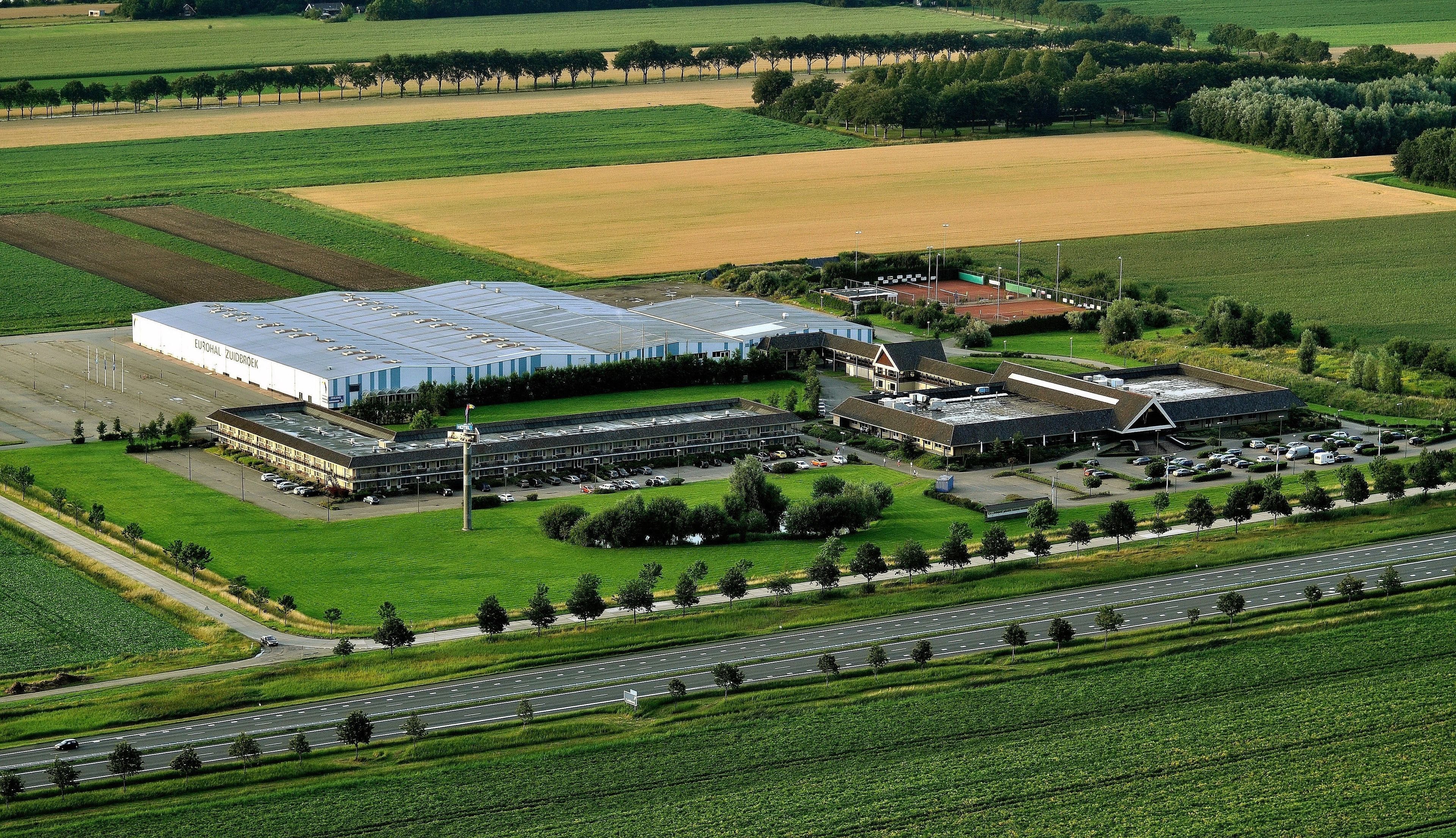 Un gran complejo industrial con varias edificaciones, zonas de estacionamiento y campos verdes aledaños.