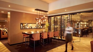 Un área de bar moderna con mostrador de madera, diversas opciones de asientos y una vinoteca al fondo.