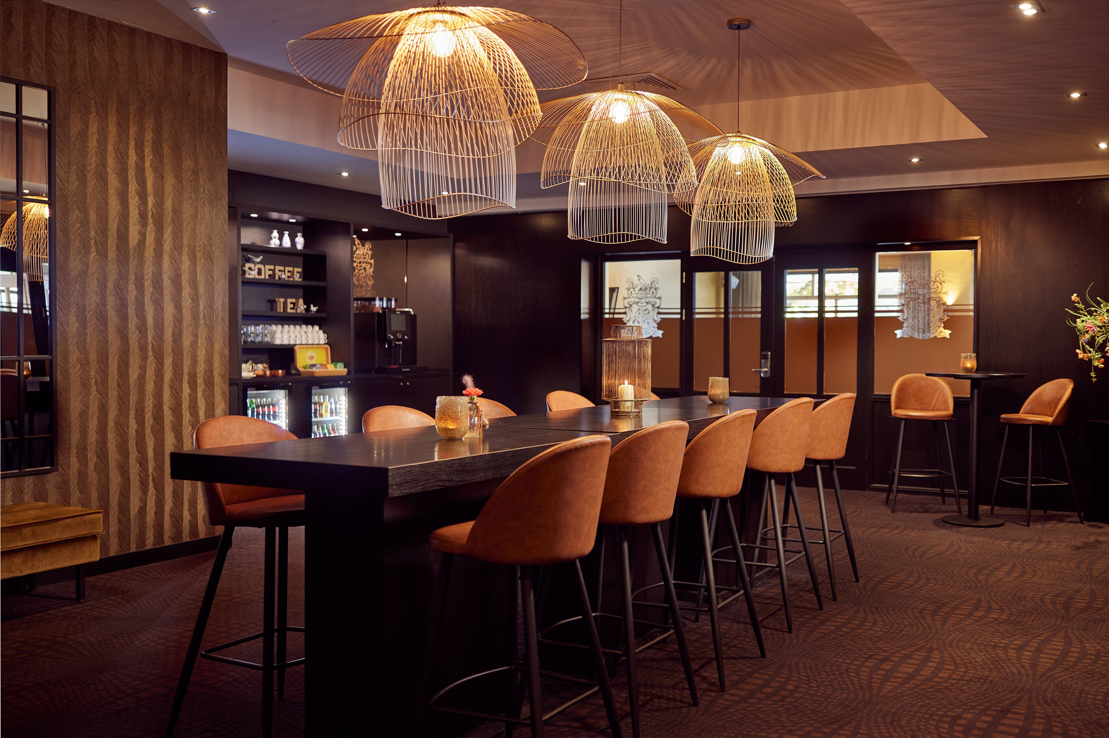 Un área de bar moderna con una barra alargada, varios taburetes y lámparas colgantes.